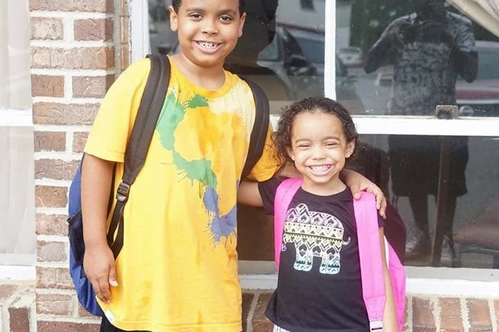 Two children smiling with the book bags they were given at a C.A.N. give-away